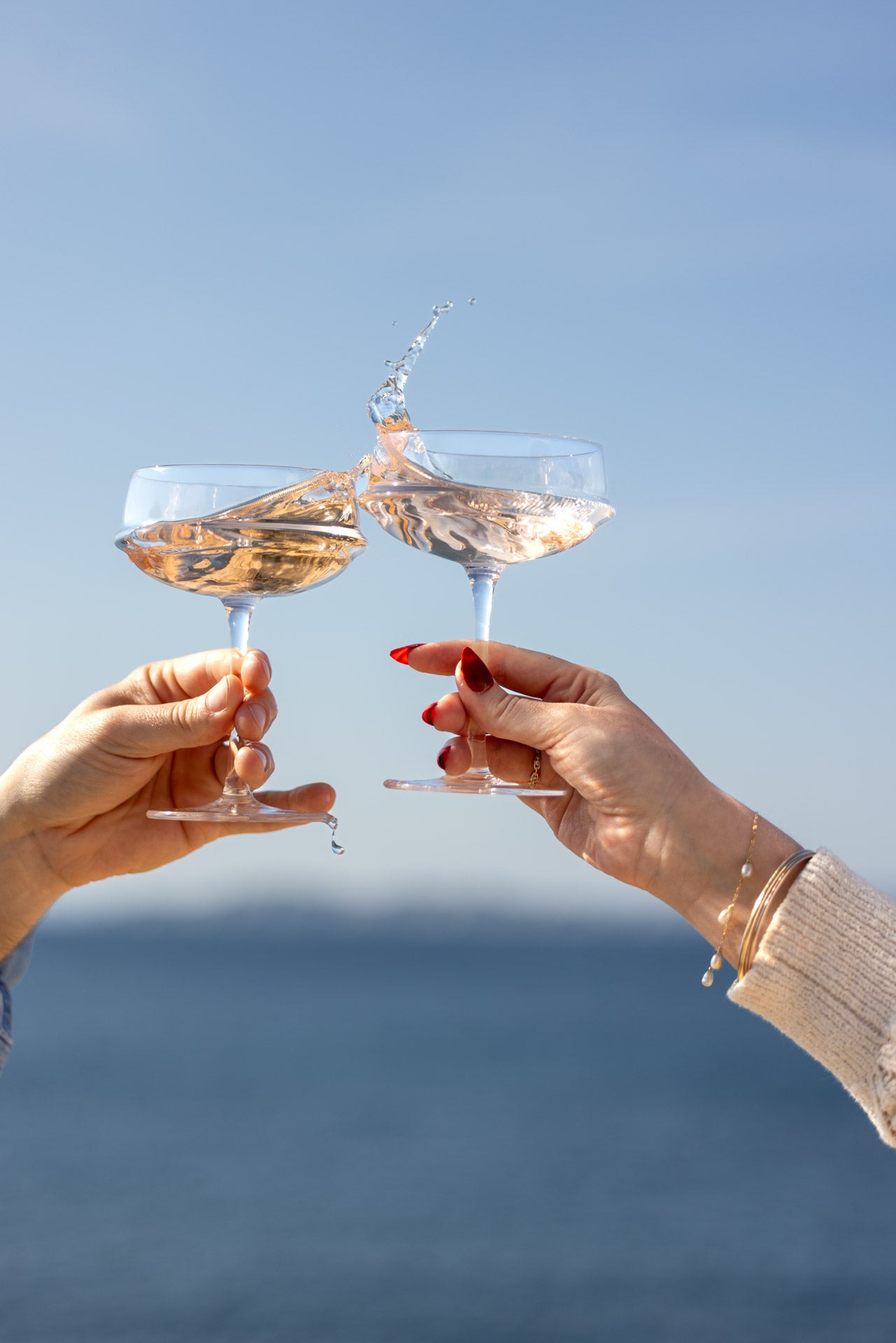 Two hands clinking rosé glasses with splash by the sea