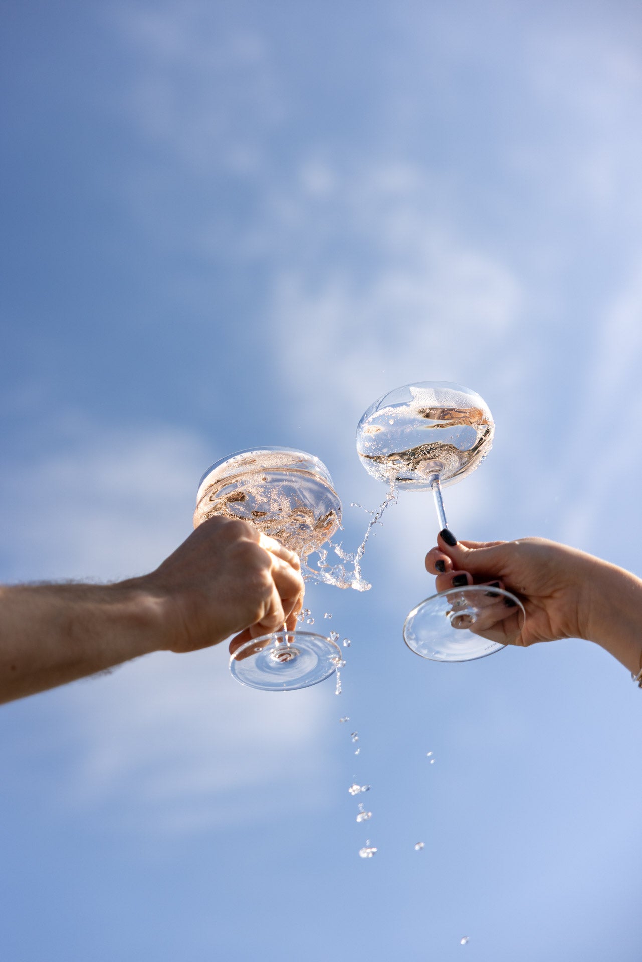 Toasting wine glasses with splash under blue sky